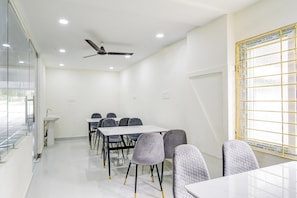A conference room with a white table, grey chairs, a ceiling fan, and a window with a grid pattern. - Super Townhouse Oak Kamineni Bus Stop (Hyderabad)