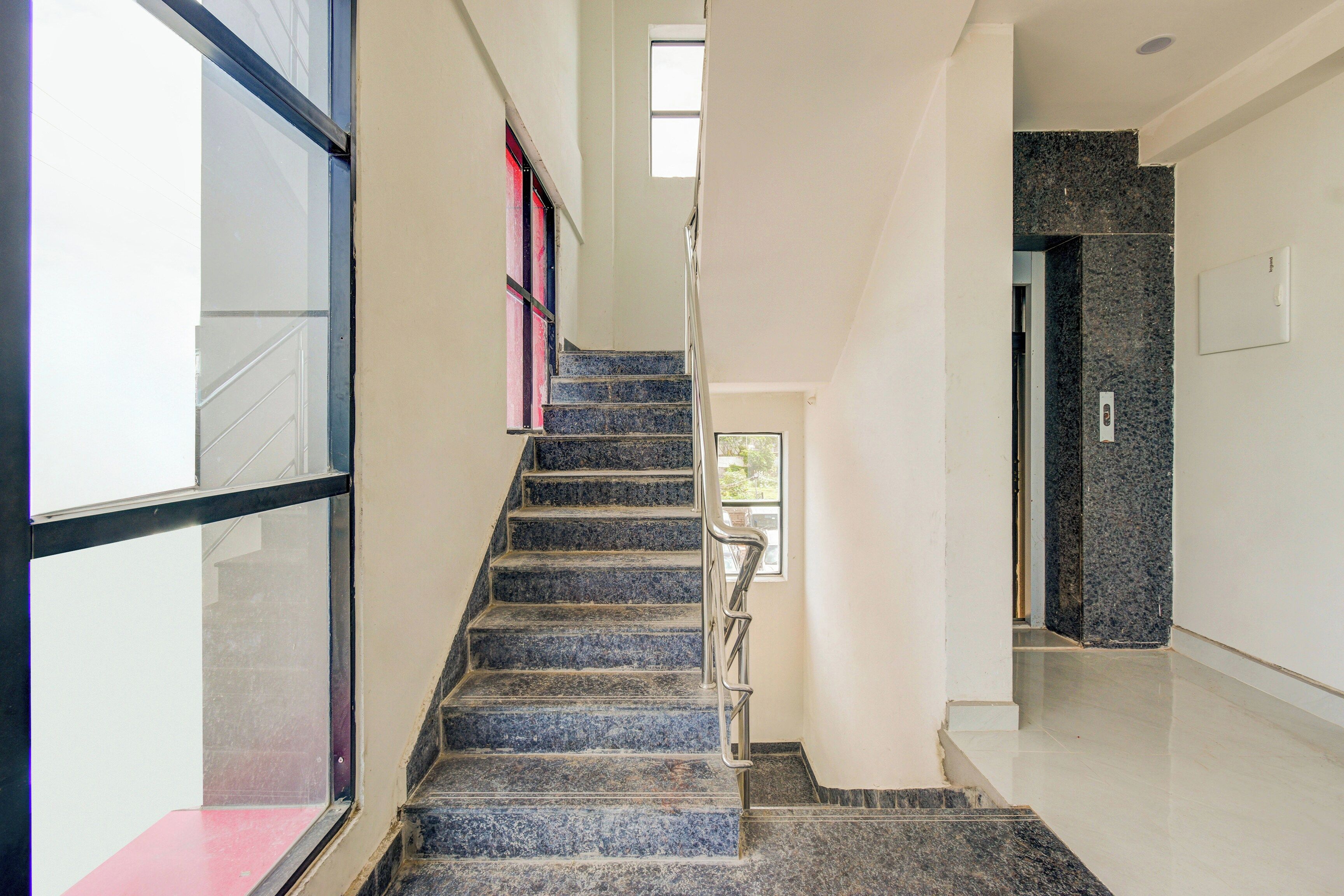 A staircase with a handrail, leading to a landing with a door and a light switch.