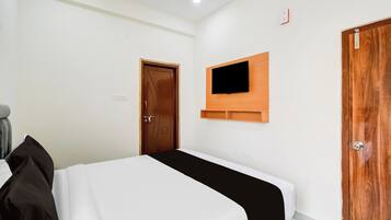 Habitación de hotel con cama, televisor montado en la pared y puerta de madera.