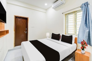 A hotel room with a bed, a TV, a window with curtains, and a wall-mounted air conditioner. - Super Townhouse Oak Kamineni Bus Stop (Hyderabad)