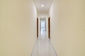 Un pasillo largo y estrecho con paredes blancas y un suelo brillante, que conduce a una puerta al final.
