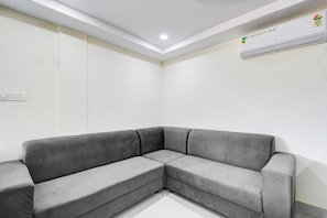 A corner room with a grey sectional sofa, a white ceiling, and an air conditioning unit. - Super Townhouse Oak Kamineni Bus Stop (Hyderabad)