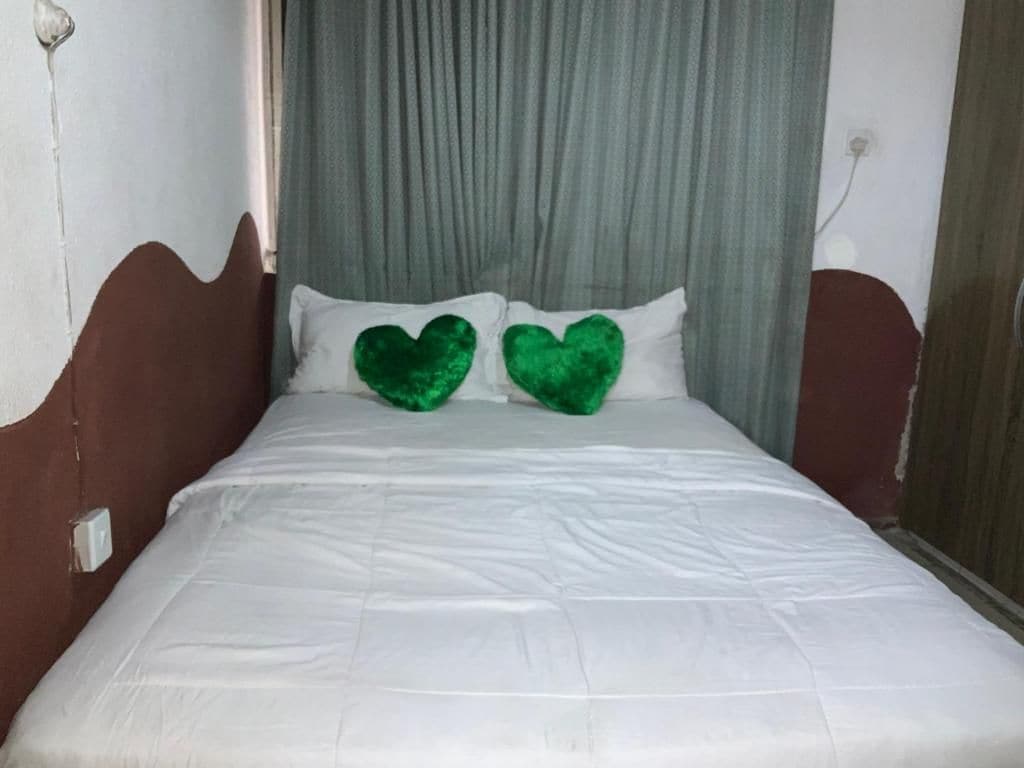 Een bed met wit beddengoed en twee groene hartvormige kussens.