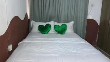 Een bed met wit beddengoed en twee groene hartvormige kussens.