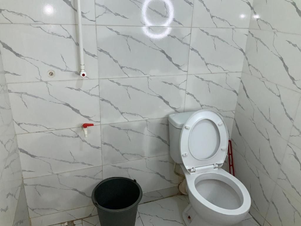 Een badkamer met een toilet, een emmer en een wand met een marmerpatroon.