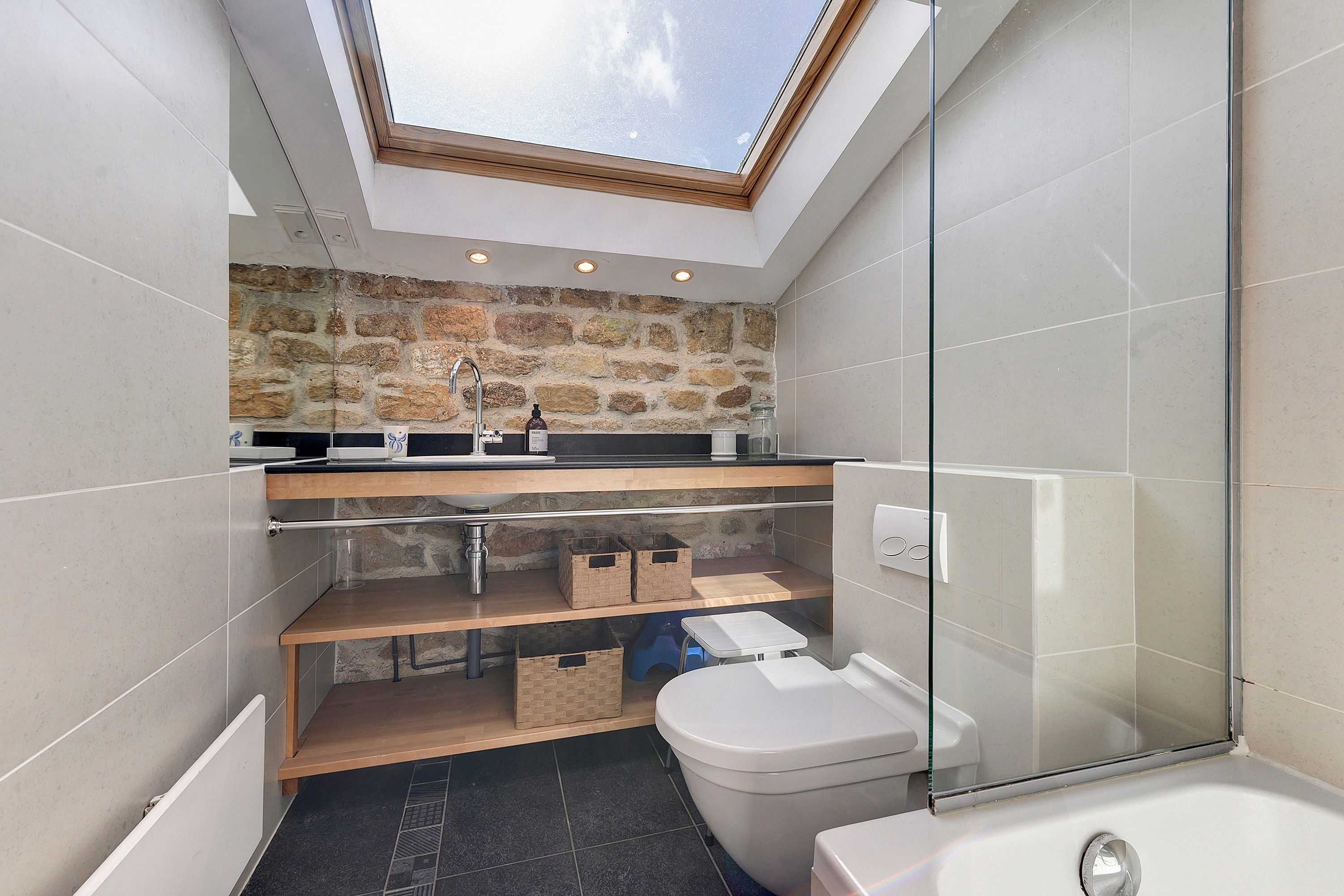 Un bagno moderno con finestra a lucernario, parete in pietra e cabina doccia in vetro.
