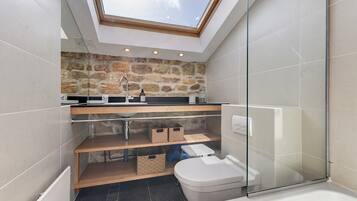 Un bagno moderno con finestra a lucernario, parete in pietra e cabina doccia in vetro.