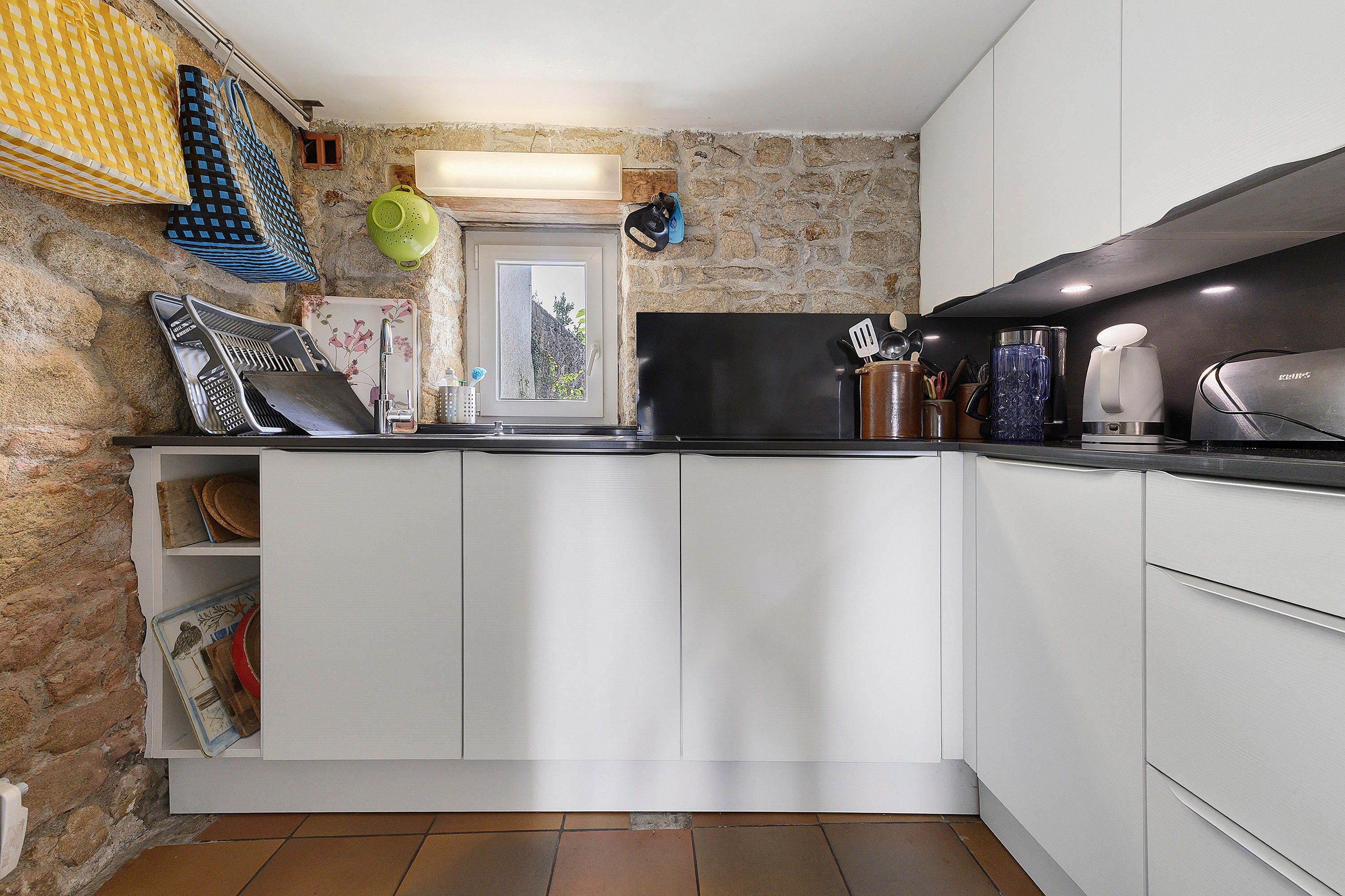 Une cuisine compacte avec des meubles blancs, une cuisinière noire et une fenêtre donnant sur un espace verdoyant.