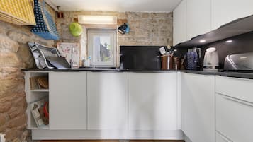 Une cuisine compacte avec des meubles blancs, une cuisinière noire et une fenêtre donnant sur un espace verdoyant.