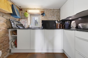 A compact kitchen with white cabinets, a black stove, and a window with a view of greenery.