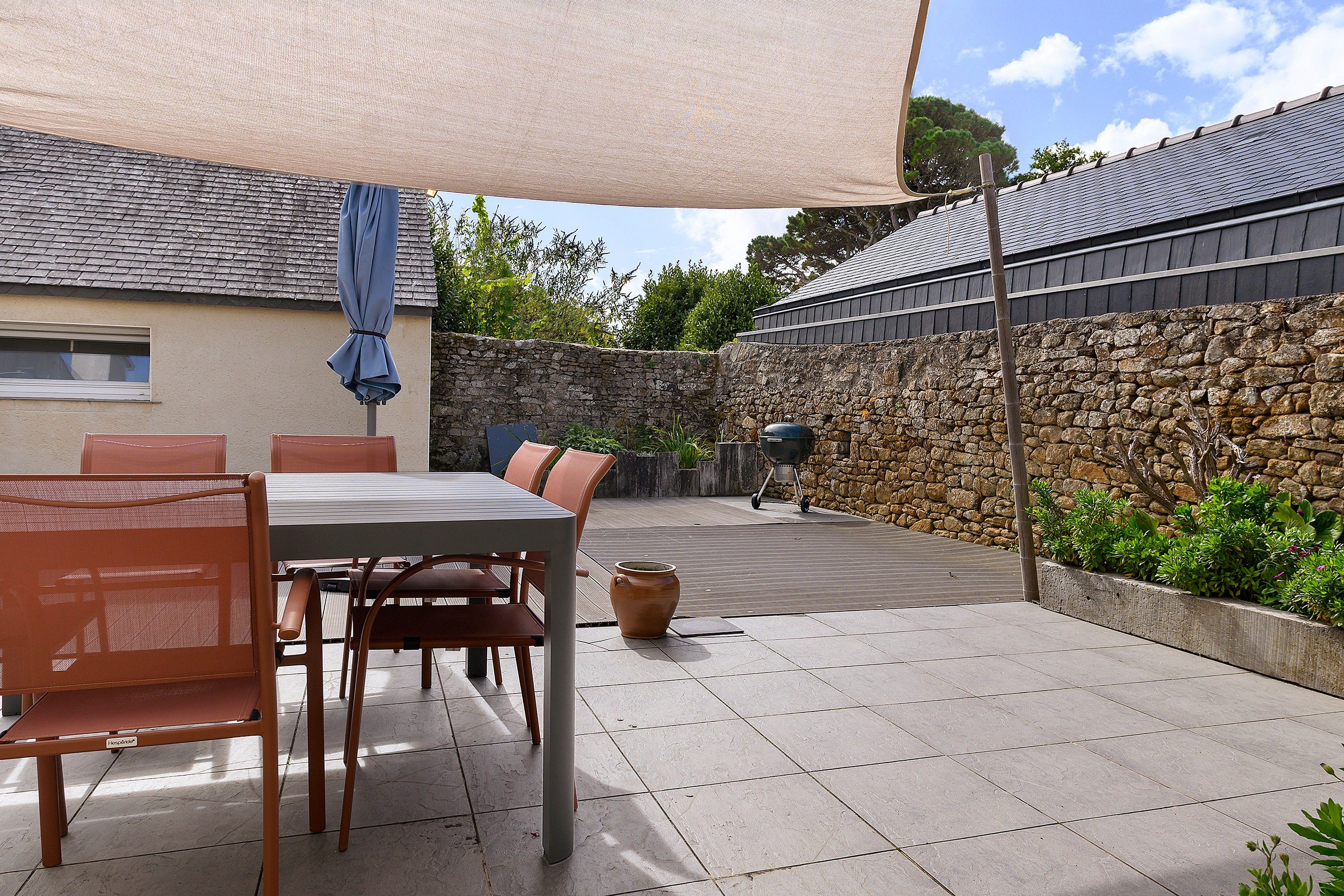 An outdoor patio area with a table and chairs, a covered seating area, and a stone wall.