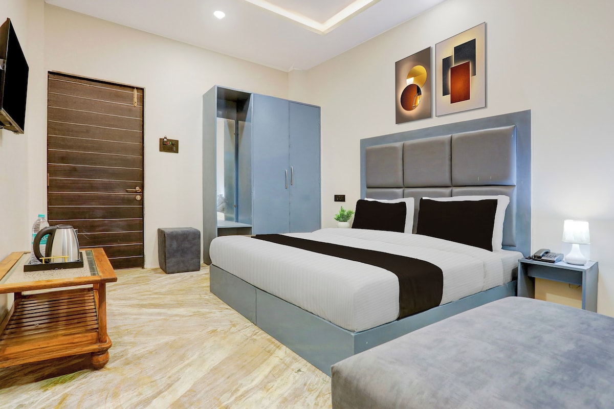 Een moderne hotelkamer met een groot bed, een nachtkastje met lamp, een klein tafeltje met waterkoker, een kledingkast en een aan de muur bevestigde televisie.