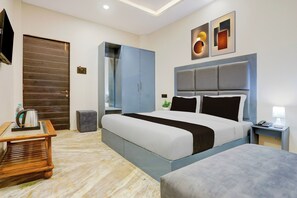 Een moderne hotelkamer met een groot bed, een nachtkastje met lamp, een klein tafeltje met waterkoker, een kledingkast en een aan de muur bevestigde televisie.