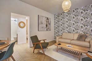En moderne stue med sofa, sofabord og lænestol. Et billede hænger på væggen, og tapetet har et mønster.