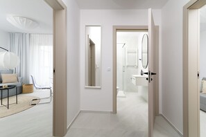 A modern interior with a hallway leading to a bathroom, a living area with a sofa and a lamp, and a view of the bathroom through a door.