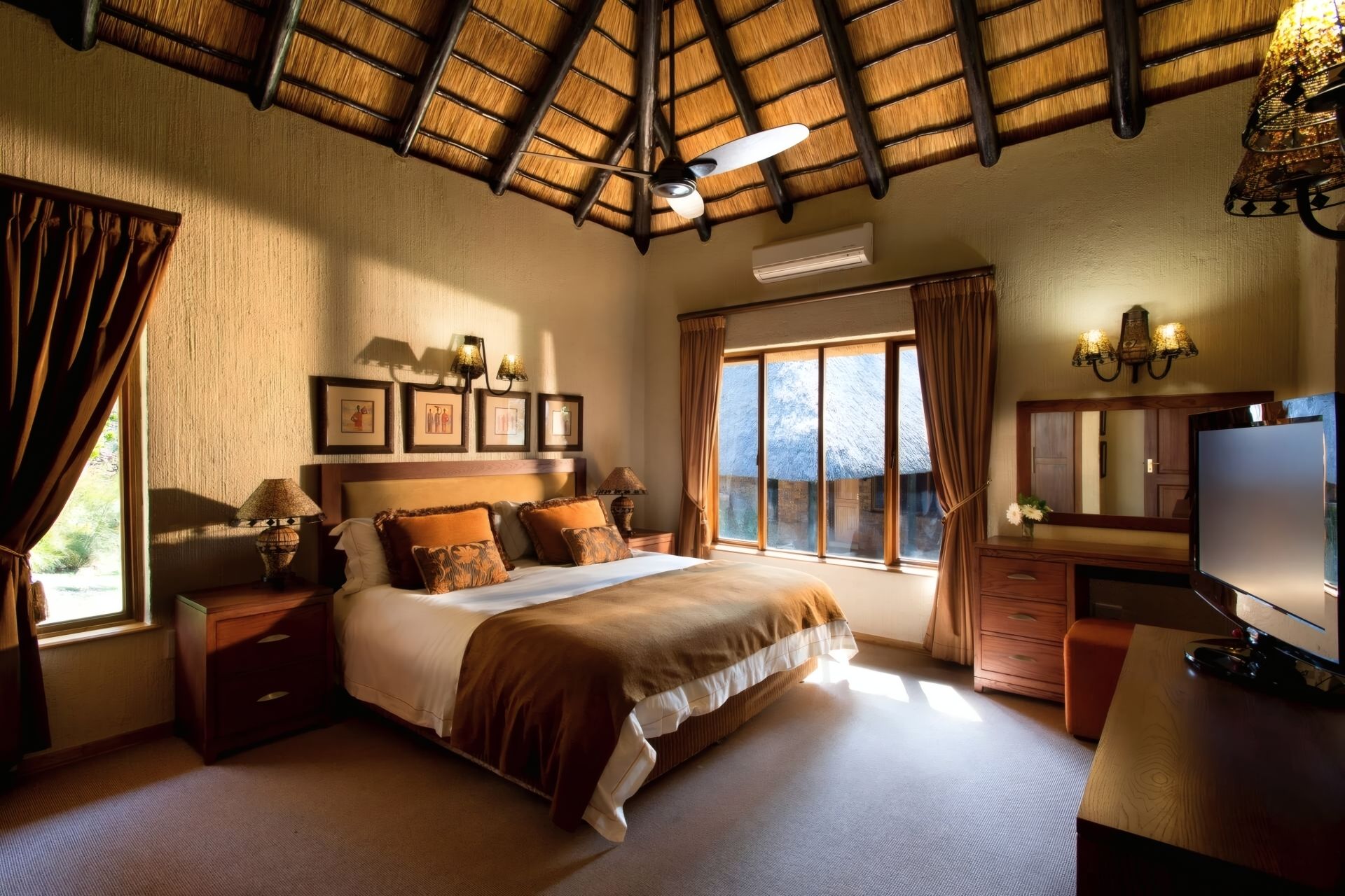 A hotel room with a bed, bedside tables, a TV, a wardrobe, and a large window with curtains.