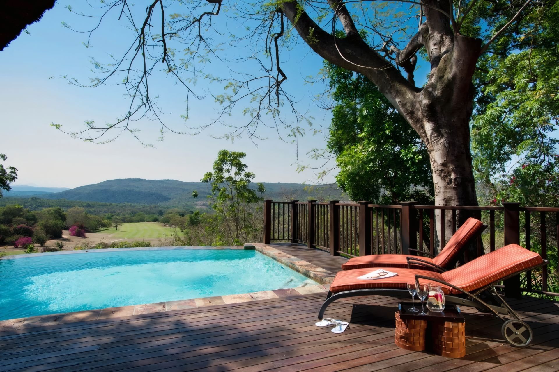 Zona junto a la piscina con terraza de madera, sillas de descanso y vistas al paisaje.