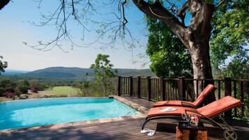 Zona junto a la piscina con terraza de madera, sillas de descanso y vistas al paisaje.