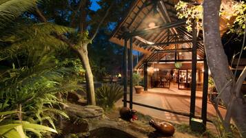 A building with a covered outdoor area, surrounded by tropical vegetation and a small water feature with hippo statues.