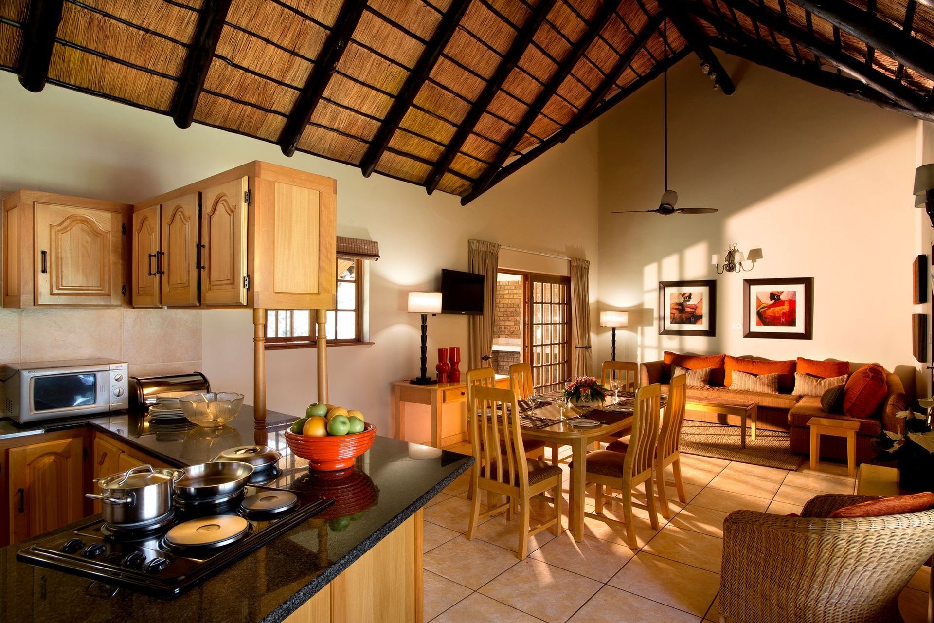 A kitchen with a microwave, stove, and wooden cabinets. There is a dining area with a table, chairs, and a sofa.