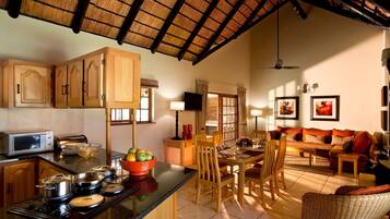 A kitchen with a microwave, stove, and wooden cabinets. There is a dining area with a table, chairs, and a sofa.