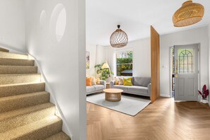 Eine Treppe mit einem strukturierten Teppich, ein Wohnzimmer mit einem grauen Sofa, einem Holztisch und einem großen Fenster mit Blick auf Grünflächen.