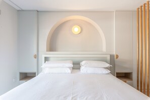 Ein modernes Schlafzimmer mit einem großen Bett, einer gewölbten Wandgestaltung und einer runden Leuchte darüber.