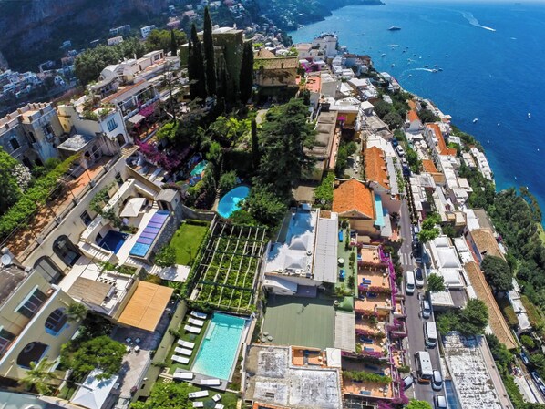 Vista aérea de un pueblo costero con una piscina destacada, viviendas densas y una vista despejada del mar.