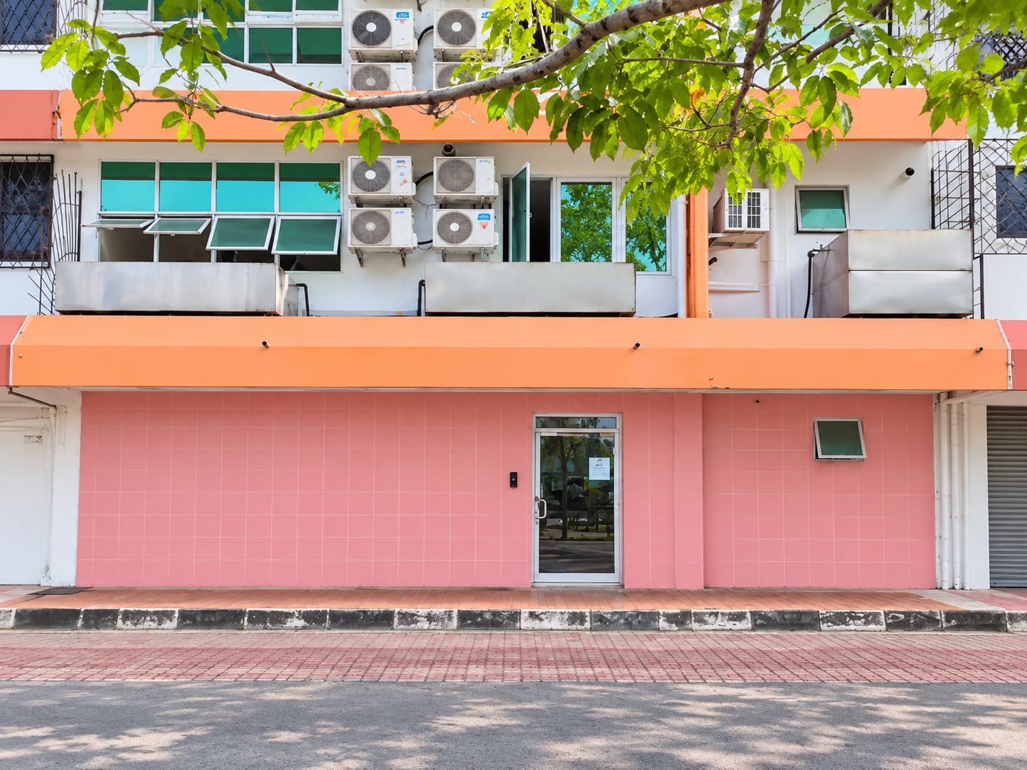 A building with a pink facade, multiple air conditioning units, and a visible entrance.