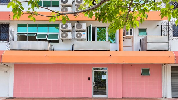 A building with a pink facade, multiple air conditioning units, and a visible entrance. - Red Tomato Hotel - self check in (Labuan)