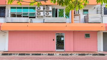 A building with a pink facade, multiple air conditioning units, and a visible entrance.