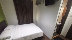 A single bed with a white mattress and pillows, a dark headboard, a brown curtain, a wall-mounted air conditioning unit, a television, and a small bathroom with a sink and mirror. - Red Tomato Hotel - self check in (Labuan)
