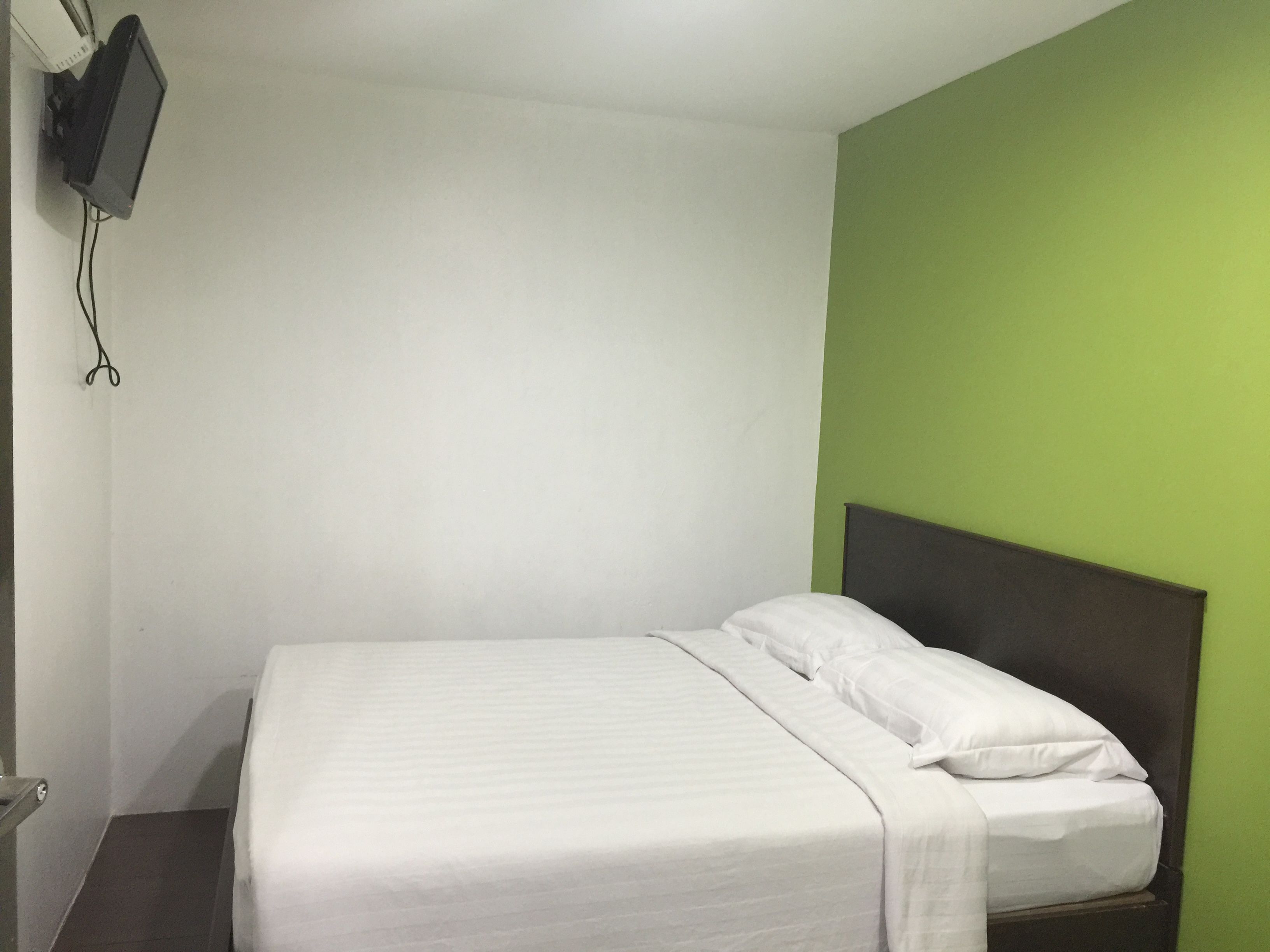 A single bed with white bedding in a room with a green accent wall and a mounted television.