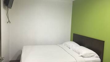 A single bed with white bedding in a room with a green accent wall and a mounted television.