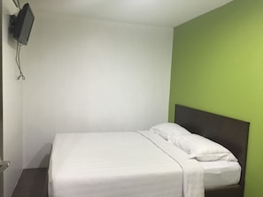 A single bed with white bedding in a room with a green accent wall and a mounted television. - Red Tomato Hotel - self check in (Labuan)