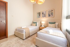 Habitación de hotel con dos camas, una puerta de madera, una mesita de noche con lámpara y tres cuadros abstractos en la pared.