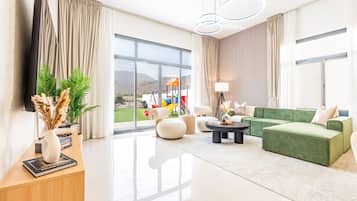 Una sala de estar moderna con un sofá verde, una mesa de centro y vista a un parque infantil a través de grandes ventanales.