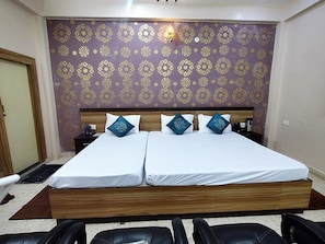 A double bed with white linens and decorative pillows, a wooden headboard, and a patterned wall. - Hotel Pratap (Etawah)
