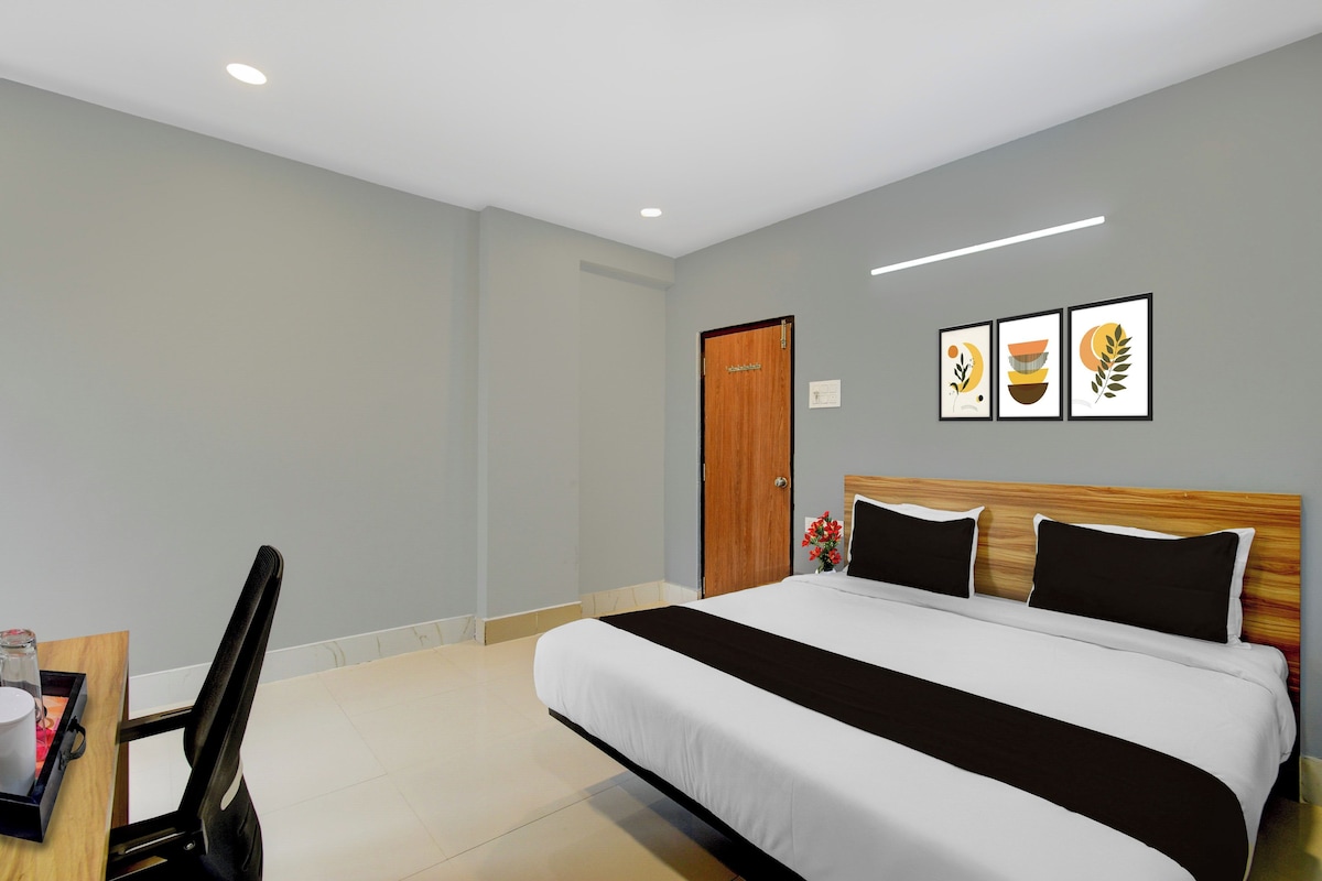 A hotel room with a bed, a desk, and a chair. There are three framed pictures on the wall.