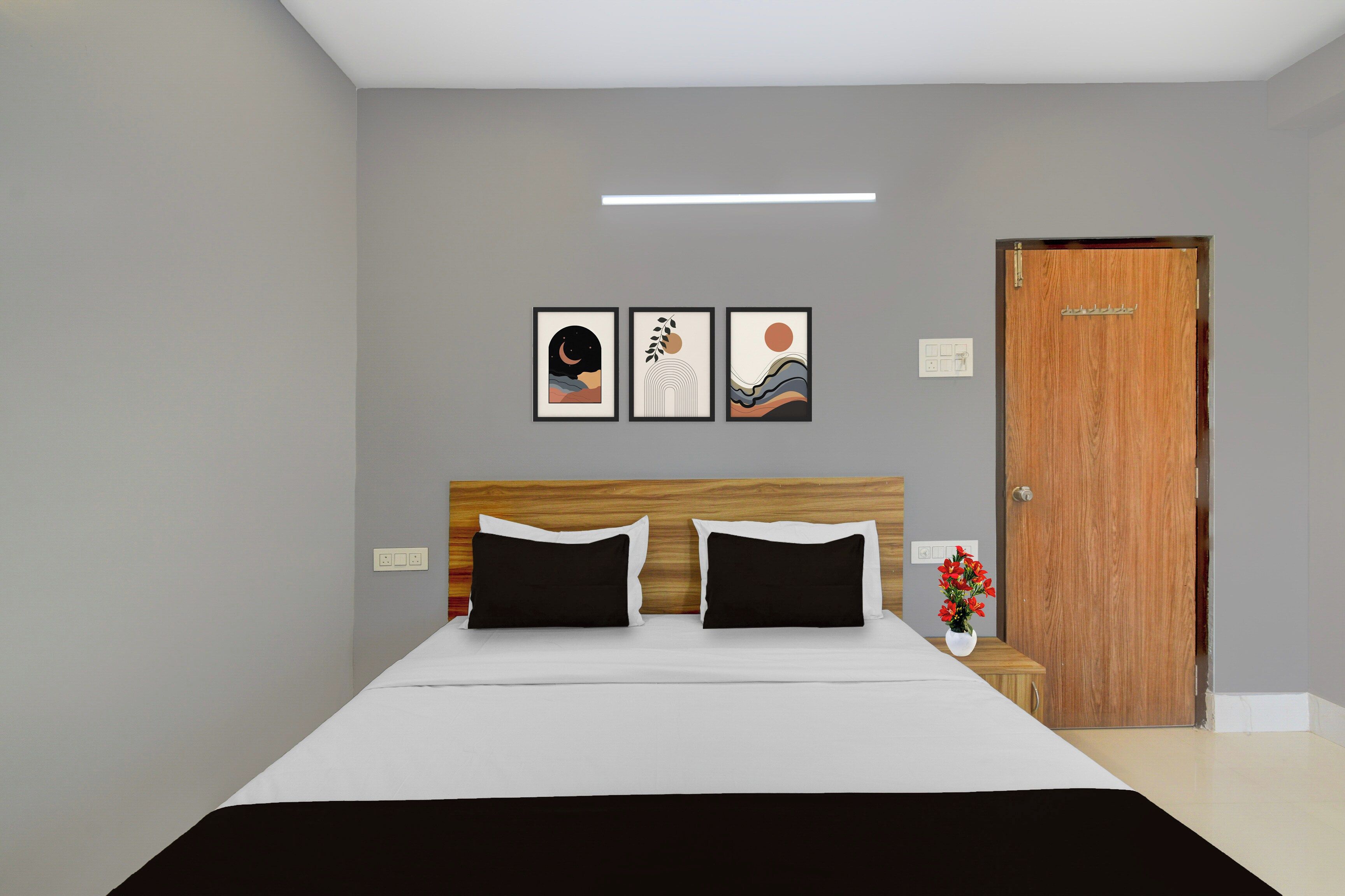 Un dormitorio con cama, cabecero de madera, mesita de noche, una puerta y tres cuadros en la pared.
