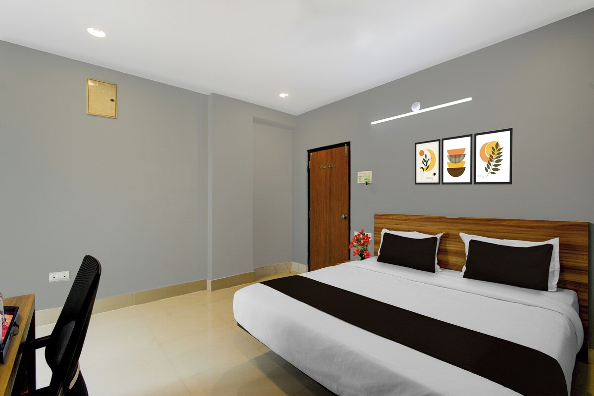 Quarto de hotel com cama, escrivaninha e cadeira. Três quadros decoram a parede.