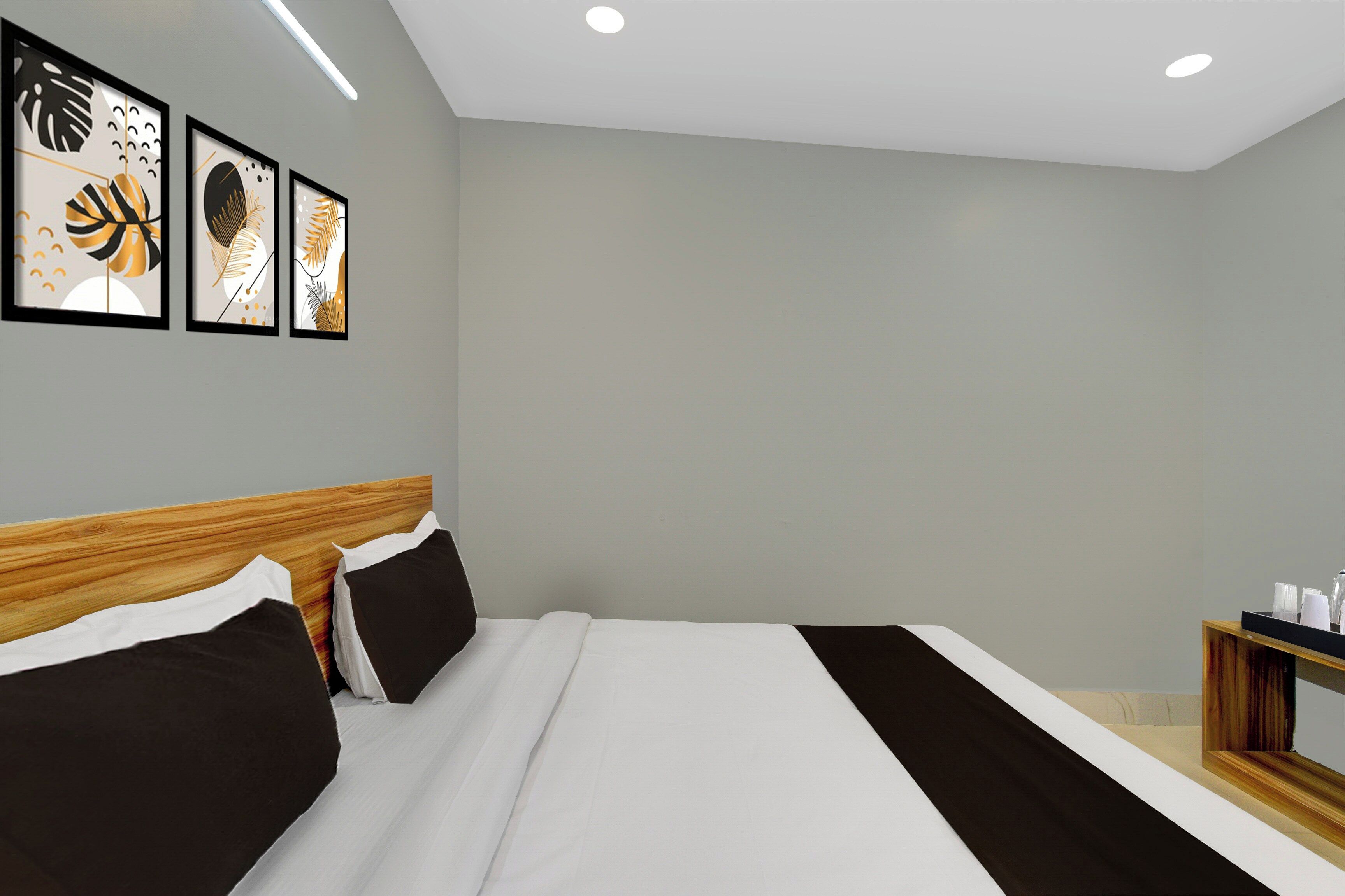 A modern hotel room with a large bed, a wooden headboard, and a bedside table with a tray of glasses.