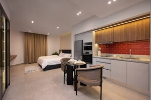 Ein modernes Hotelzimmer mit Bett, einer Essecke mit Tisch und Stühlen, einer Küche mit roten Fliesen und einem Fernseher.