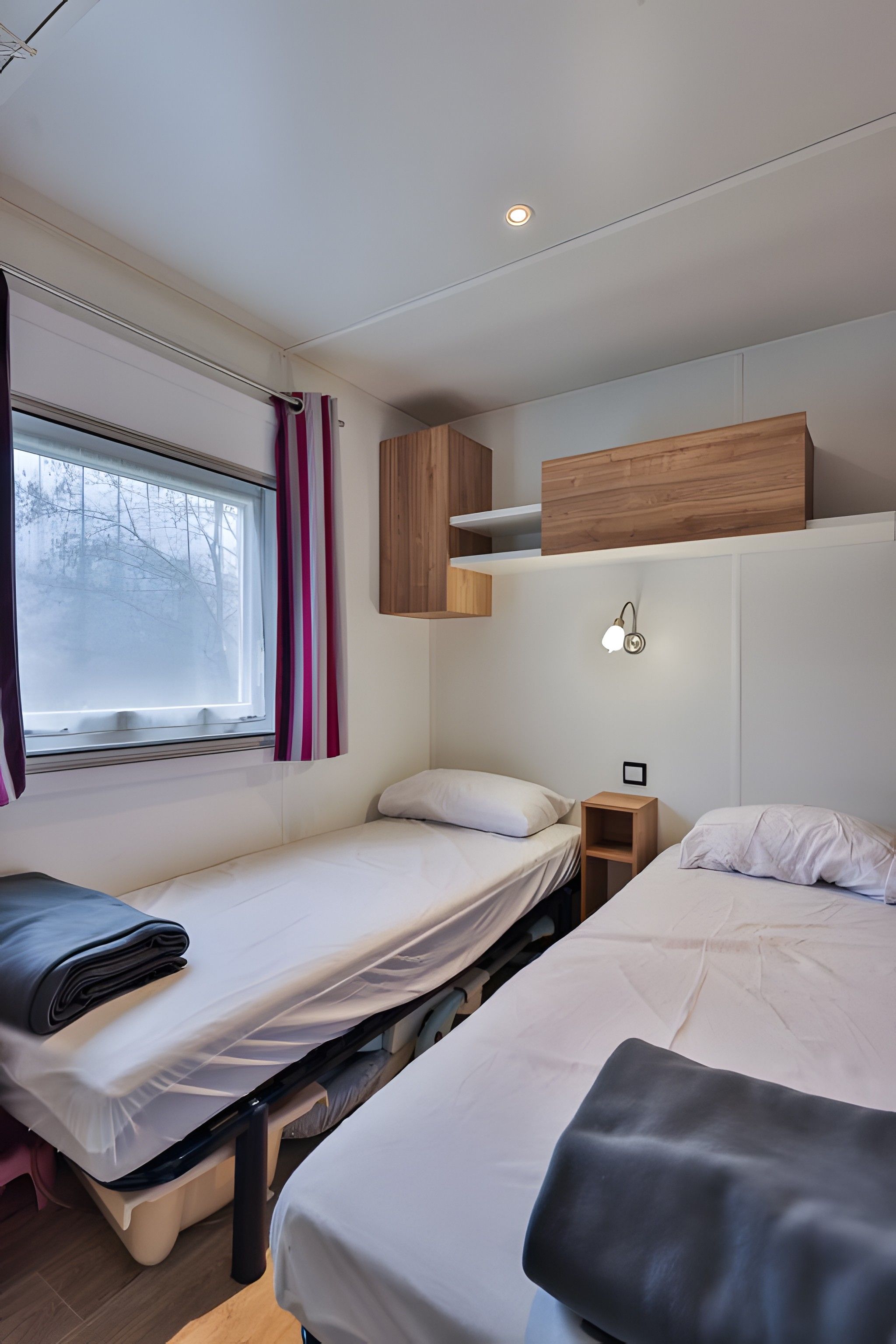 Un dormitorio con dos camas, una ventana con cortinas, una mesita de noche y un estante en la pared.