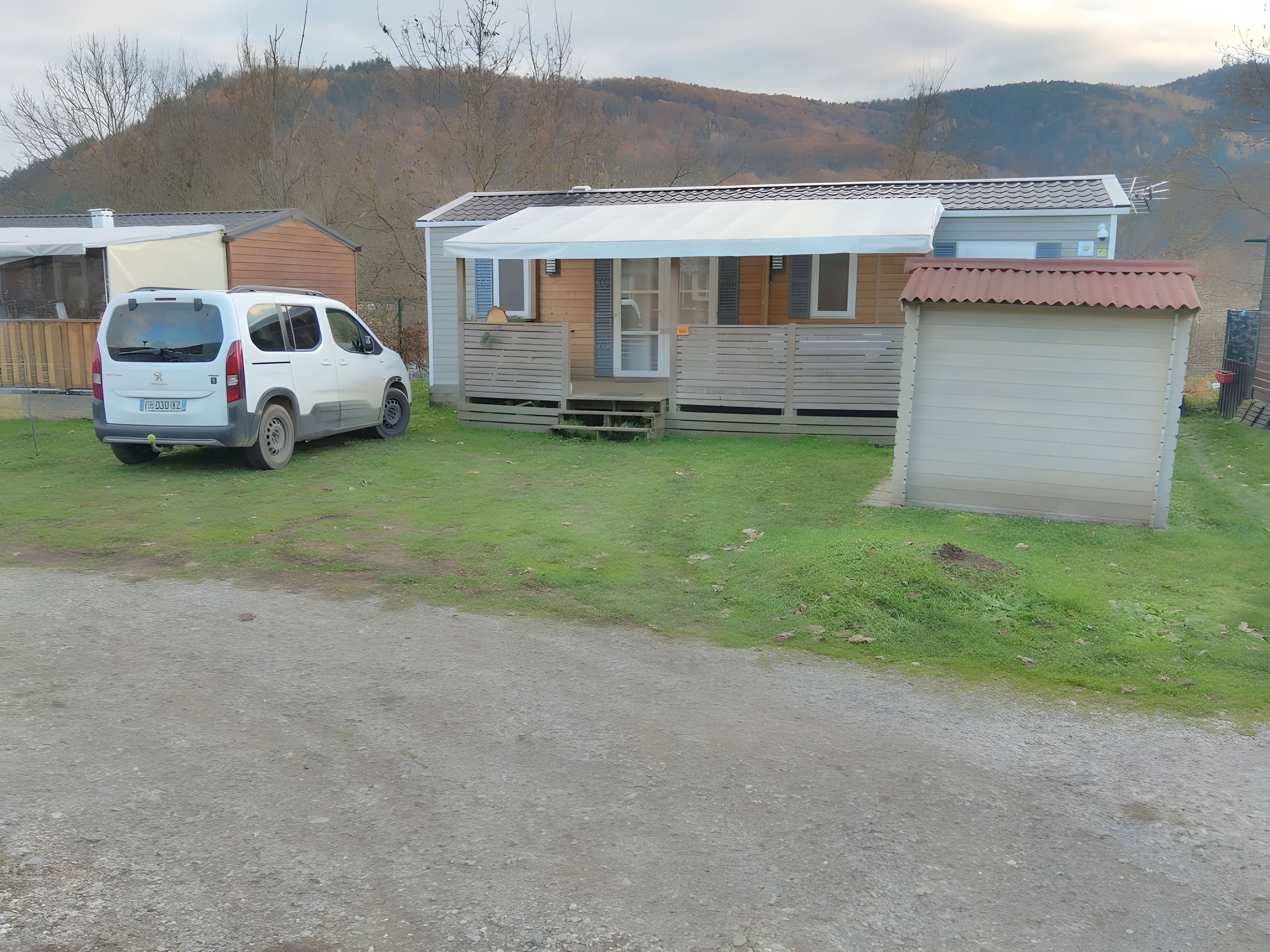 En campingvogn med en mindre tilbygning, en hvid varevogn og et indhegnet område.
