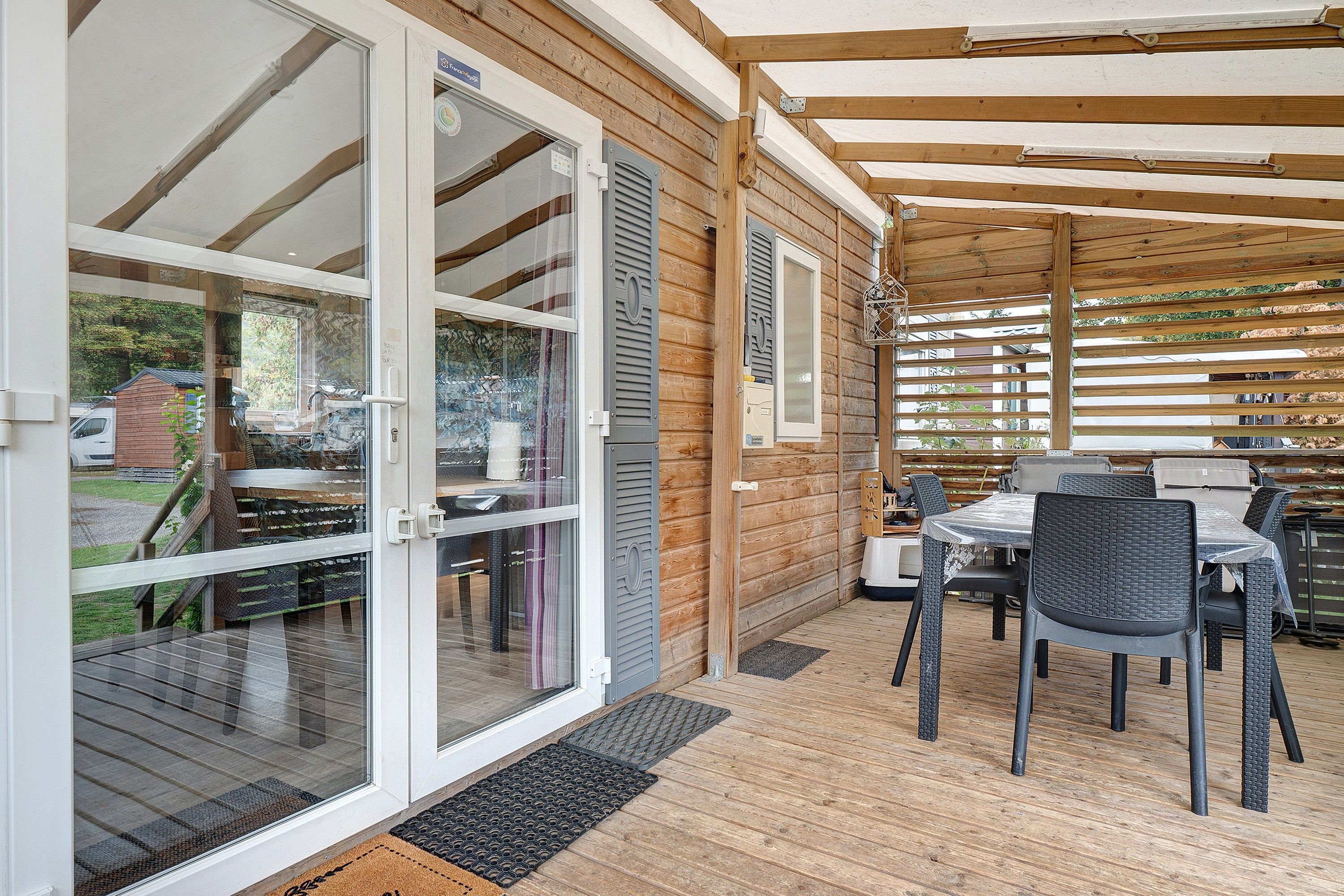 Un patio techado con mesa y sillas, una puerta corrediza de vidrio y una estructura de pérgola de madera.