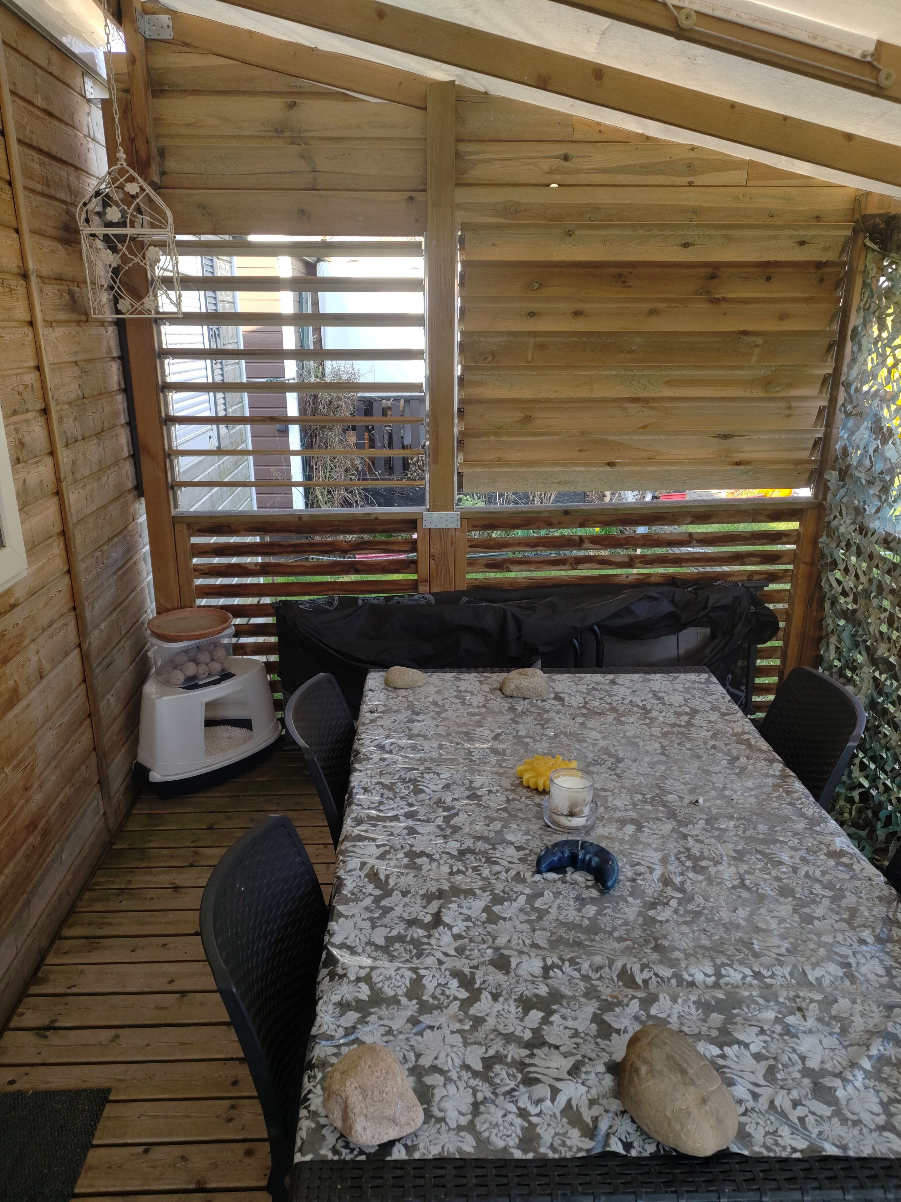 Una terraza de madera con una mesa y sillas, un comedero para pájaros y un comedero pequeño para mascotas.