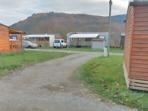 Un camino de grava que lleva a una hilera de cabañas, con montañas al fondo.