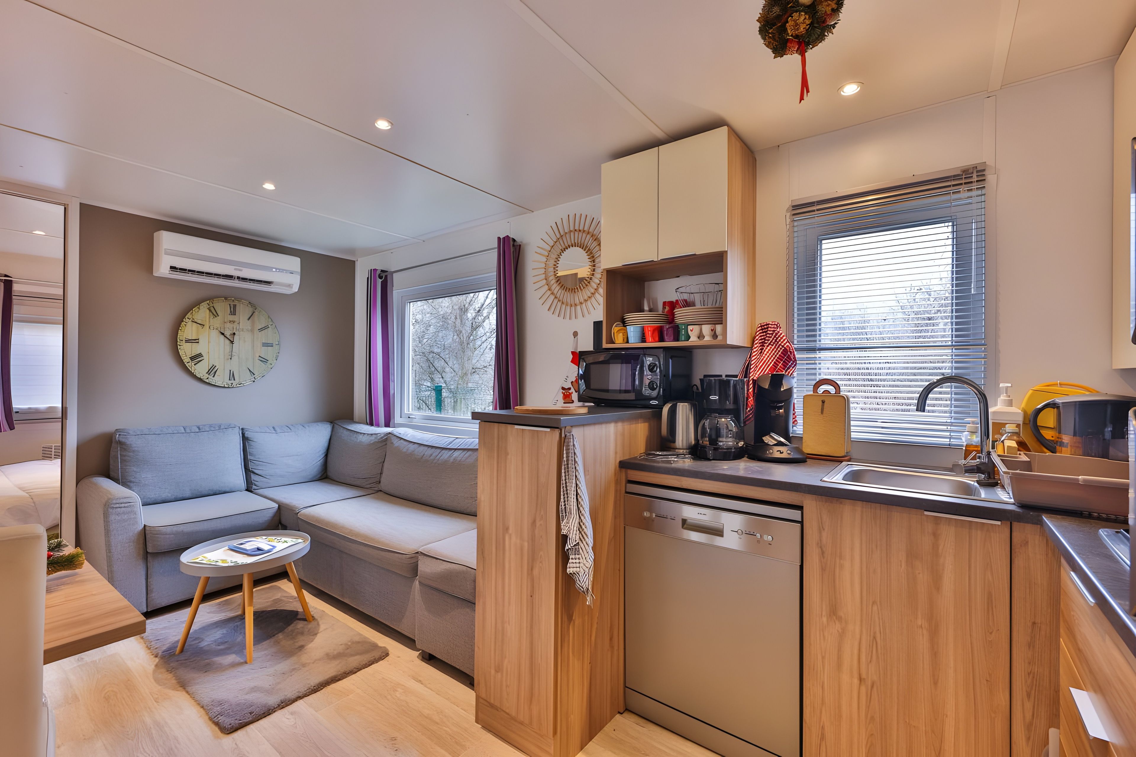 Un espacio habitable compacto con kitchenette, un sofá, una mesa de comedor y un reloj de pared grande.