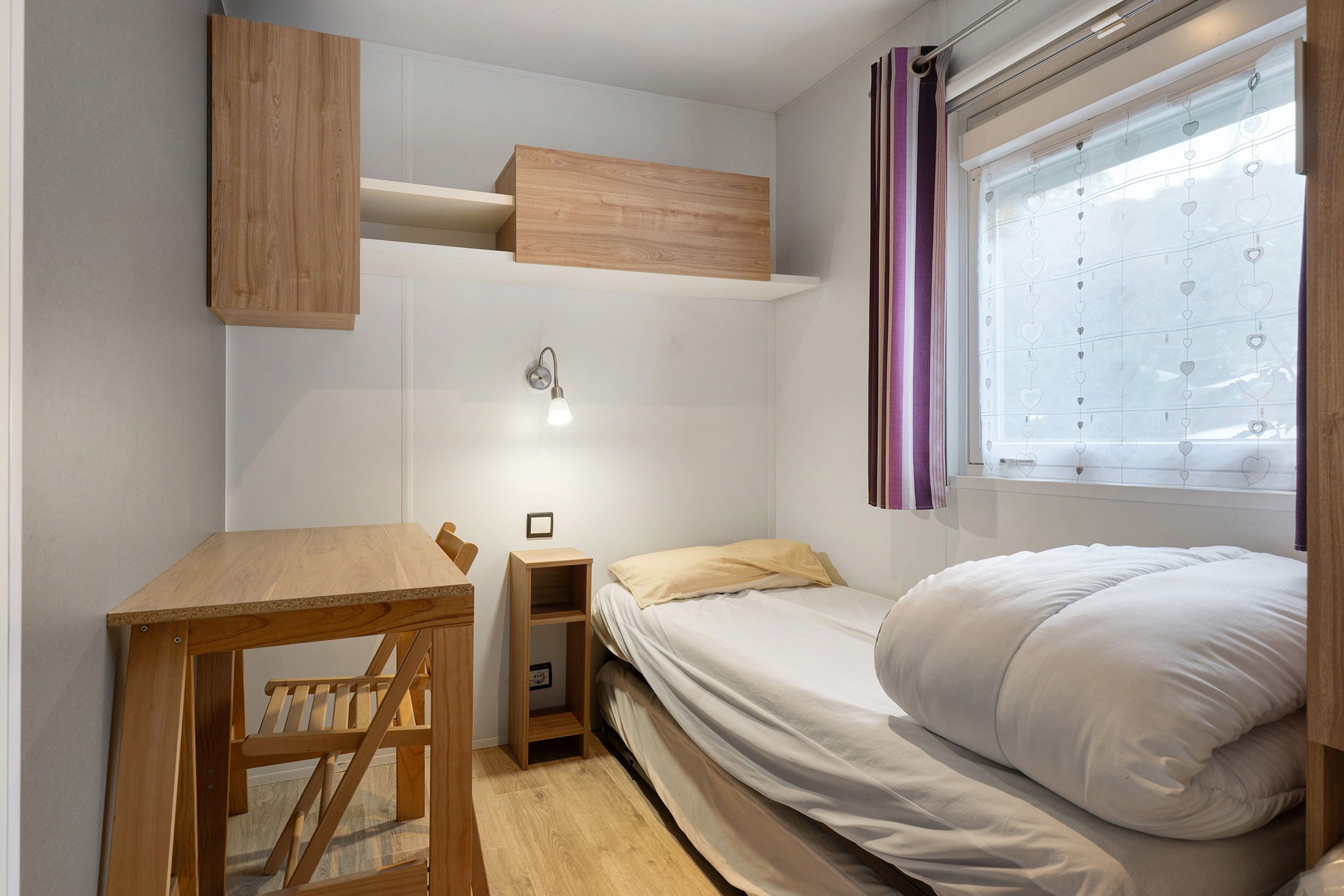Un dormitorio compacto con una cama litera, un escritorio de madera pequeño y una mesita de noche.